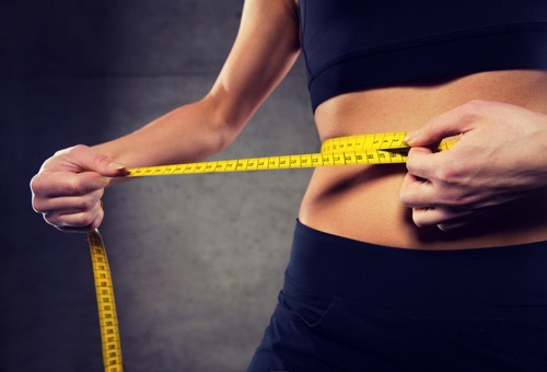 sport, fitness, weight loss, diet and people concept - close up of woman measuring waist size by tape in gym